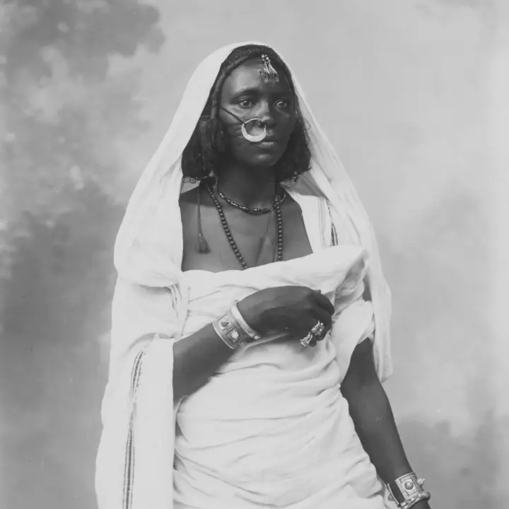 About Us Portrait of an African Woman dressed in traditional costume, wearing decorative jewelry.